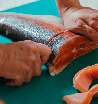 hand-cutting-raw-headless-salmon-fish-laying-on-bl-2022-05-19-15-33-07-utc.jpg